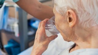 SYMBOLBILD: Eine alte Frau trinkt aus einem Glas Wasser. Vor allem bei enormer Hitze wie derzeit, aber längst nicht nur dann ist ausreichendes Trinken wichtig - doch viele Menschen in Deutschland kommen nicht auf die empfohlene Menge.