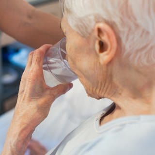 SYMBOLBILD: Eine alte Frau trinkt aus einem Glas Wasser. Vor allem bei enormer Hitze wie derzeit, aber längst nicht nur dann ist ausreichendes Trinken wichtig - doch viele Menschen in Deutschland kommen nicht auf die empfohlene Menge.