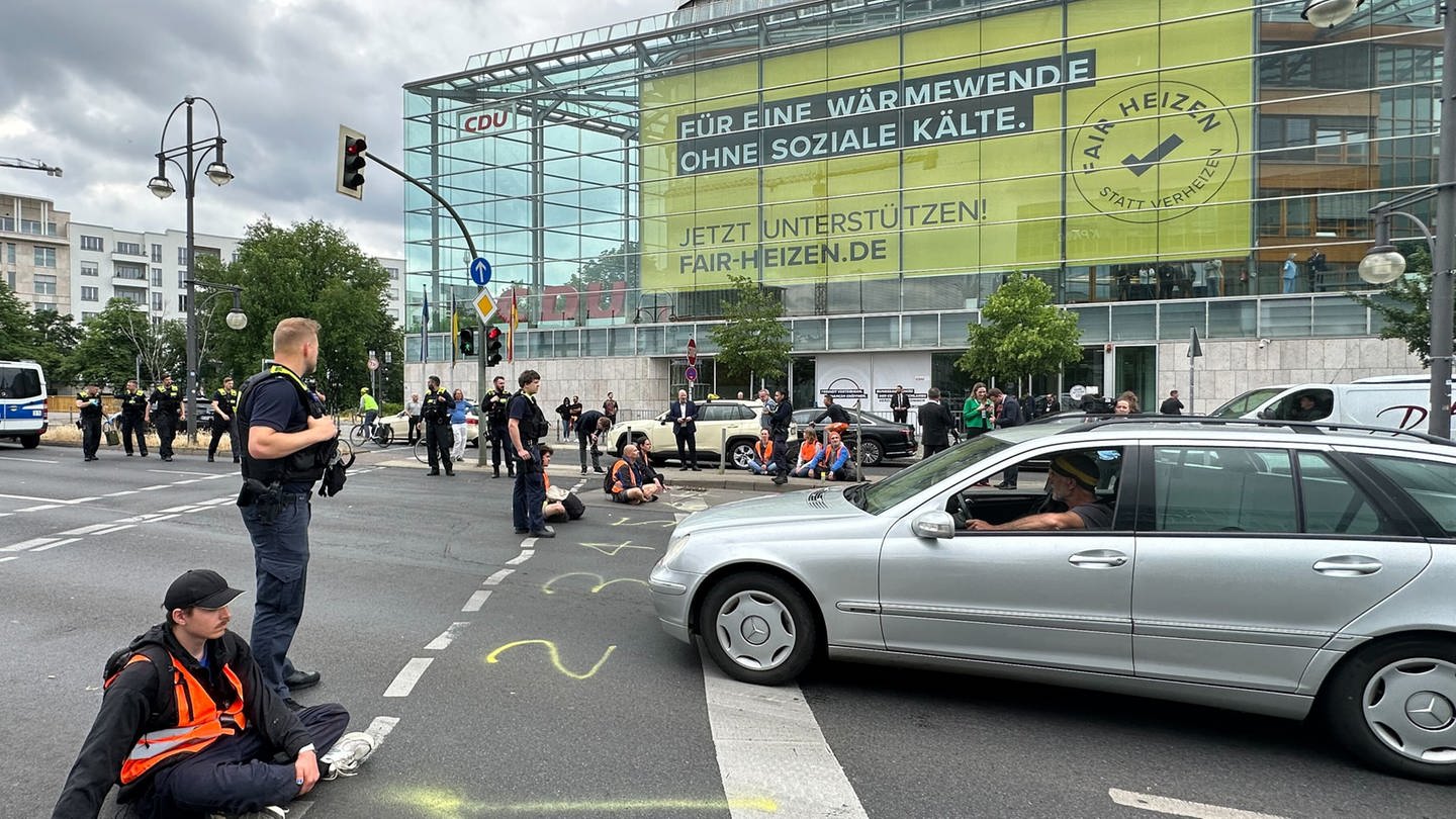 Ein Klima-Aktivist sitzt an einer Straßenkreuzung, neben ihm ein Polizist.
