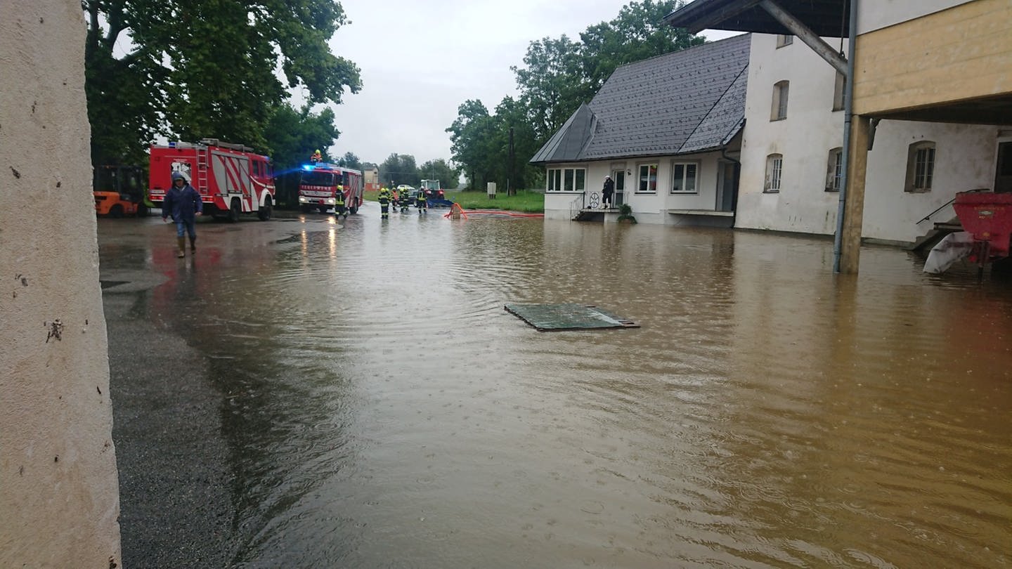 Eine Dorfstraße in Österreich ist überschwemmt, die Feuerwehr pumpt Wasser ab