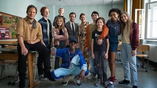 Schauspielerinnen und Schauspieler haben sich für ein Gruppenfoto im Klassenraum eingefunden, der als Drehort des Films "Das Fliegende Klassenzimmer" gedient hat.