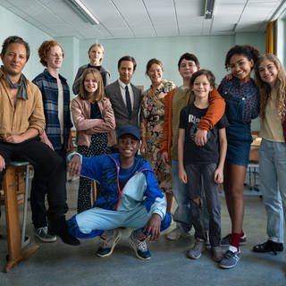 Schauspielerinnen und Schauspieler haben sich für ein Gruppenfoto im Klassenraum eingefunden, der als Drehort des Films "Das Fliegende Klassenzimmer" gedient hat.