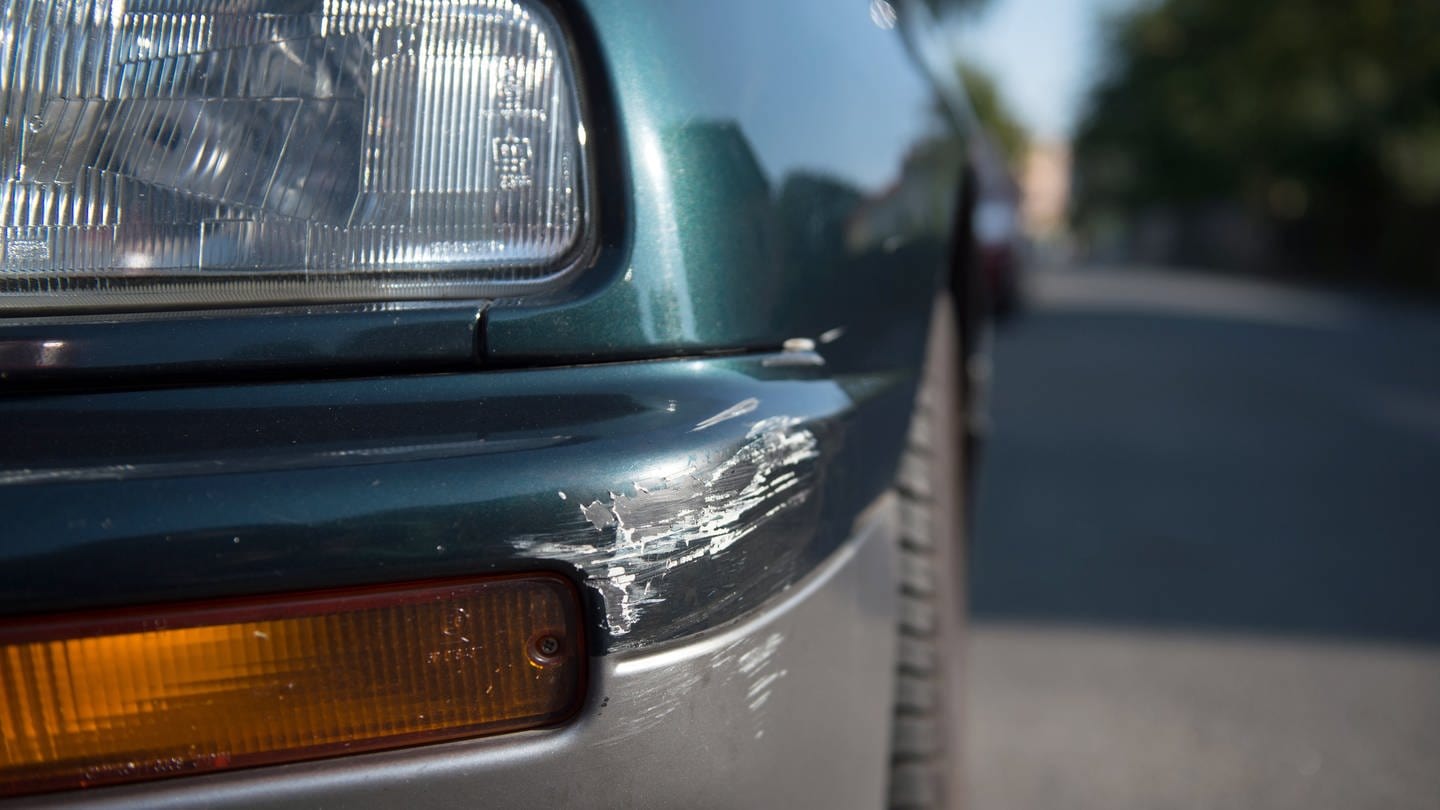 An der Ecke eines Front-Stoßfängers eines geparkten Autos sind Spuren eines Unfalls zu sehen.