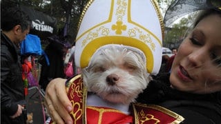 Eine Frau hält ihren kleinen Hund mit Papst-Kappe am 22.10.2016 bei einer Kostüm-Parade zum Gruselfest Halloween in New York auf dem Arm