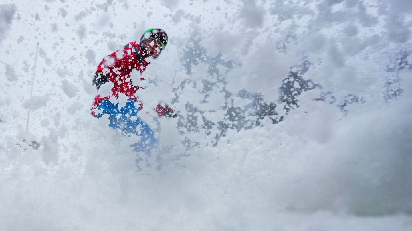 Ein Skifahrer bremst auf der Piste, durch den aufstäubenden Schnee ist er nur schemenhaft zu sehen