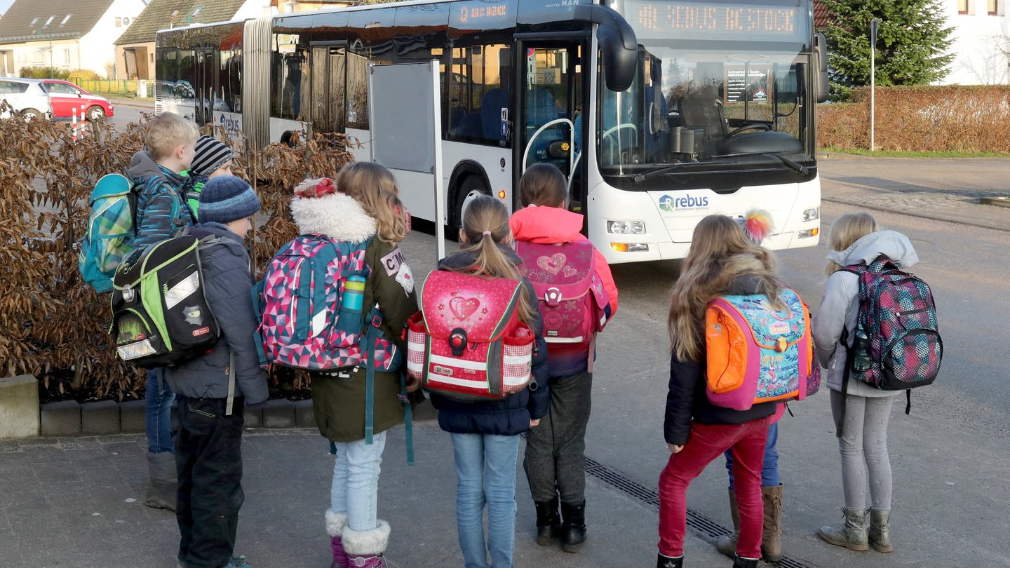 Kinder stehen vor einem Schulbus, bereit zum Einsteigen.