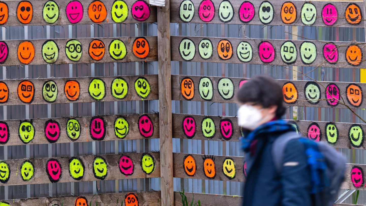 Eine Passantin mit Mund-Nasen-Bedeckung geht an einem hölzernen Bauzaun im Museumsquartier vorbei, der mit bunten Smileys bemalt wurde.