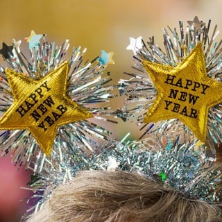 Ein Frau begrüßt das Neue Jahr mit einem Kopfschmuck mit der Aufschrift "Happy New Year".