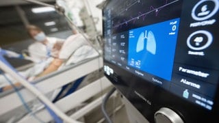 Eine Pflegerin versorgt auf einer Intensivstation eine Patientin, im Vordergrund ist der Monitor eines Beatmungsgeräts zu sehen