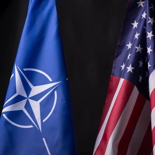 Eine Nato-Fahne und eine USA-Fahne sind auf schwarzem Hintergrund zu sehen.