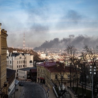 Während Altbauten unversehrt im Vordergrund zu sehen sind, steigt eine Rauchwolke über dem Kiewer Stadtteil Ljukaniwska auf.