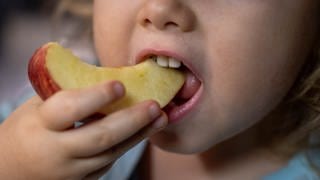 Ein Kind isst ein Stück Apfel von einem Teller mit Snacks.