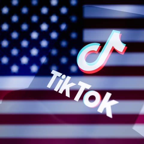 Das TikTok-Logo wird auf einem Smartphone vor dem Hintergrund der abgeschnittenen US-Fahne angezeigt.