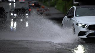 Ein Auto fährt durch eine große Wasserlache auf der Fahrbahn.