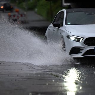 Ein Auto fährt durch eine große Wasserlache auf der Fahrbahn.