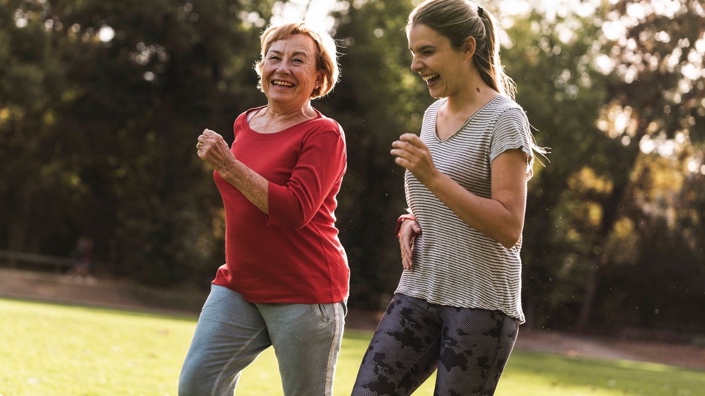Eine ältere Frau und eine jüngere joggen zusammen im Grünen.