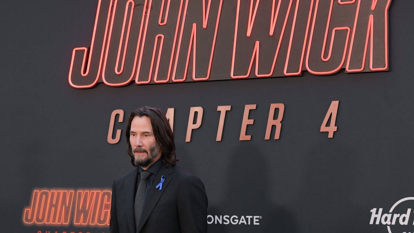 Der Schauspieler steht bei der Hollywood-Premiere von John Wick: Kapitel 4 vor dem gleichlautenden Plakat