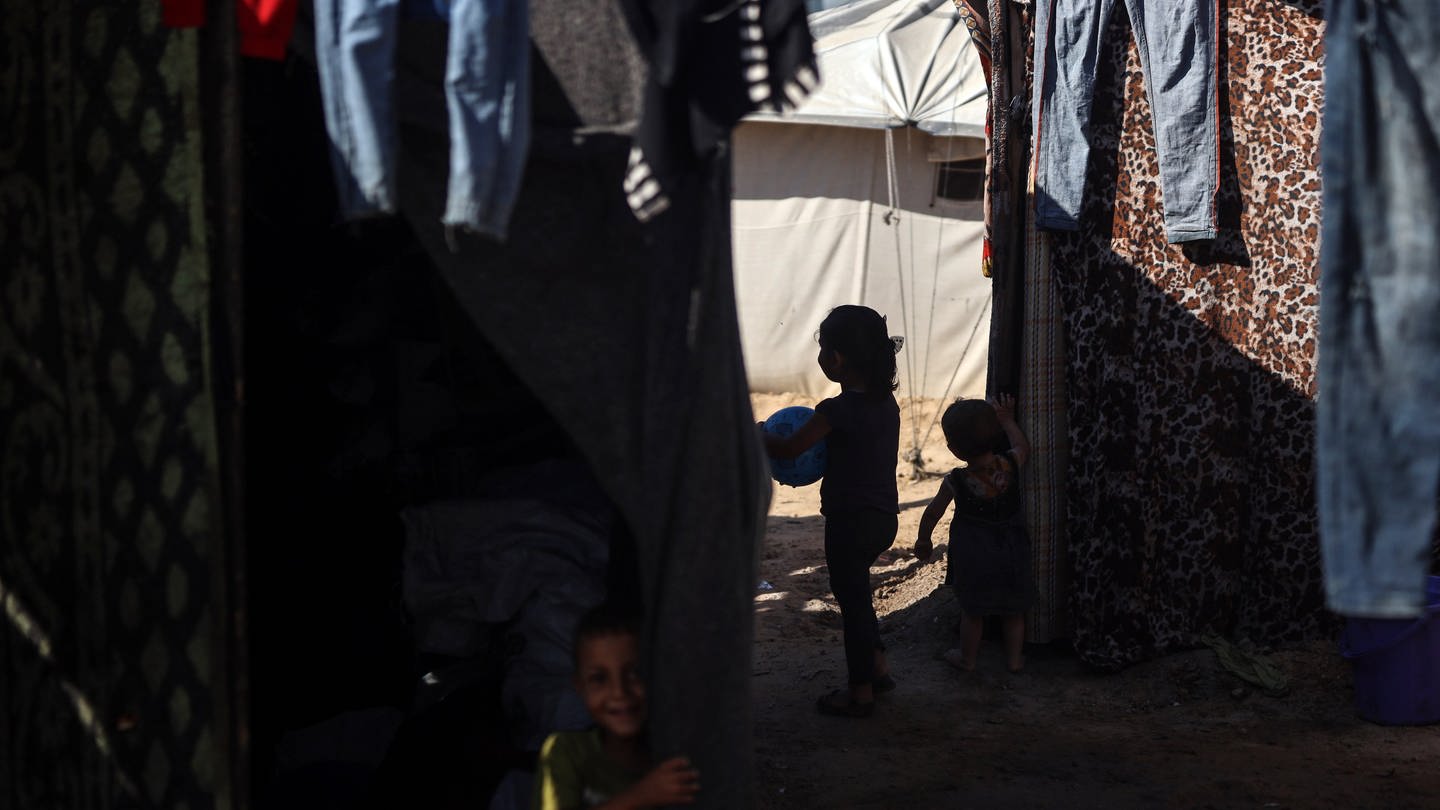 Kinder spielen in einem Flüchtlingscamp im Schatten zwischen Zelten und aufgehängter Wäsche