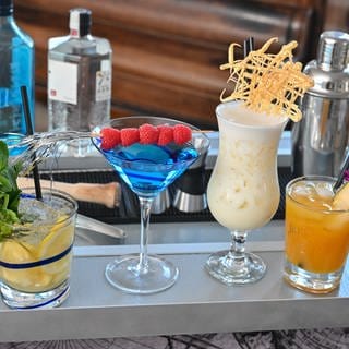 Vier verschiedene Cocktails stehen nebeneinander auf einer Bar.