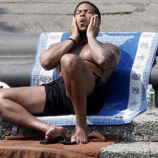 Ein Mann sitzt auf Handtüchern, die auf Stufen in einem Park ausgelegt sind, und hat T-Shirt und Schuhe in der Hitze ausgezogen.