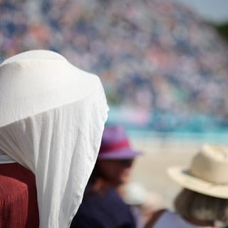 Eine Frau hat sich ein Tuch über den Hut zum Schutz vor der Sonne geworfen