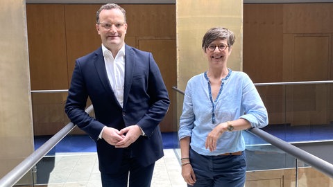 Jens Spahn und Korrespondentin Eva Ellermann stehen im ARD-Hauptstadtstudio nebeneinander und schauen in die Kamera