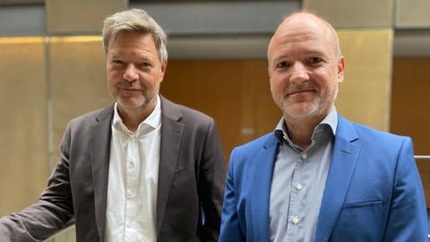 Robert Habeck und Korrespondent Jan Zimmermann stehen in der Halle des ARD-Hauptstadtstudios nebeneinander und schauen in die Kamera