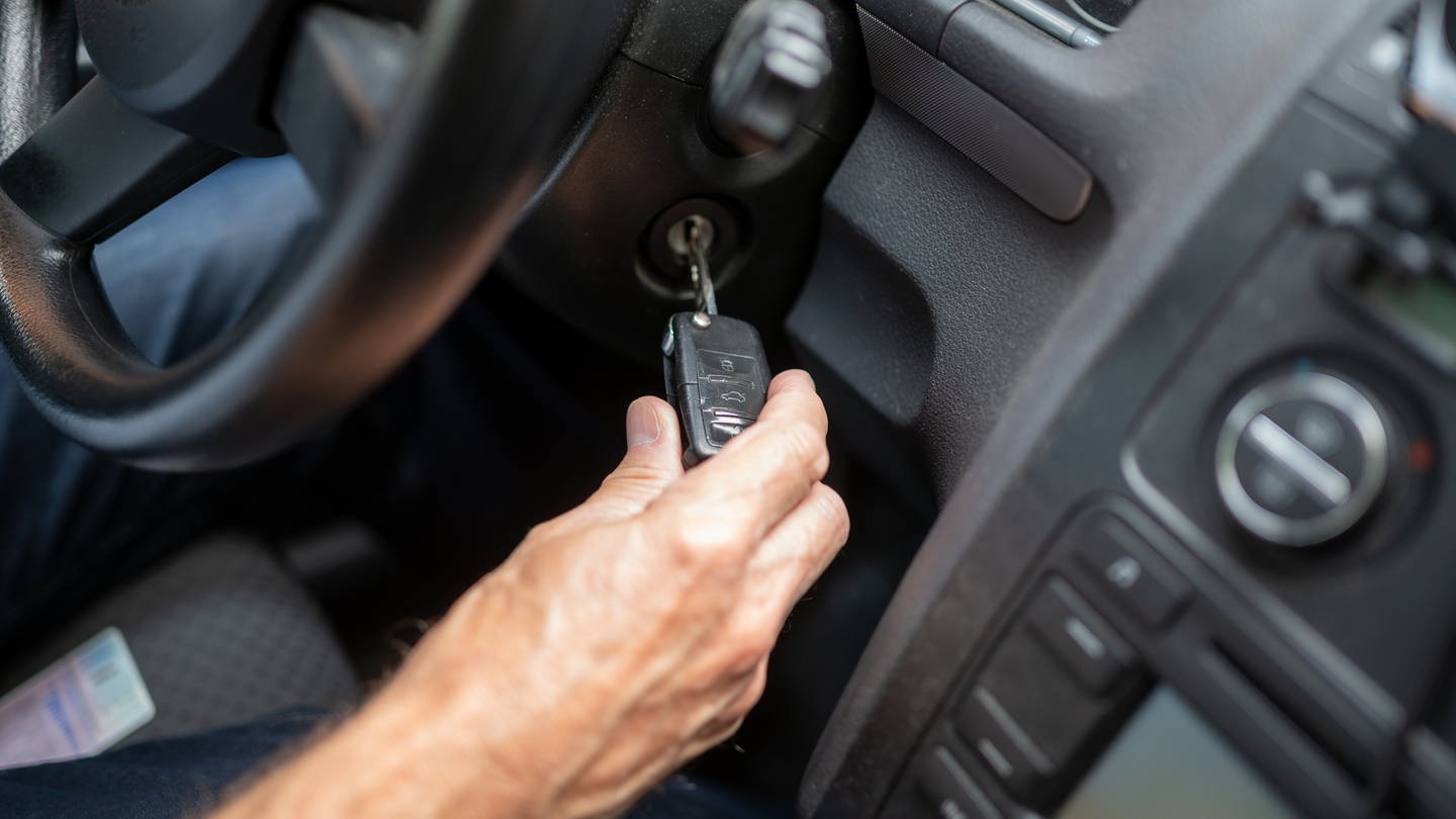 Ein älterer Mann steckt den Schlüssel in das Zündschloss eines Autos.