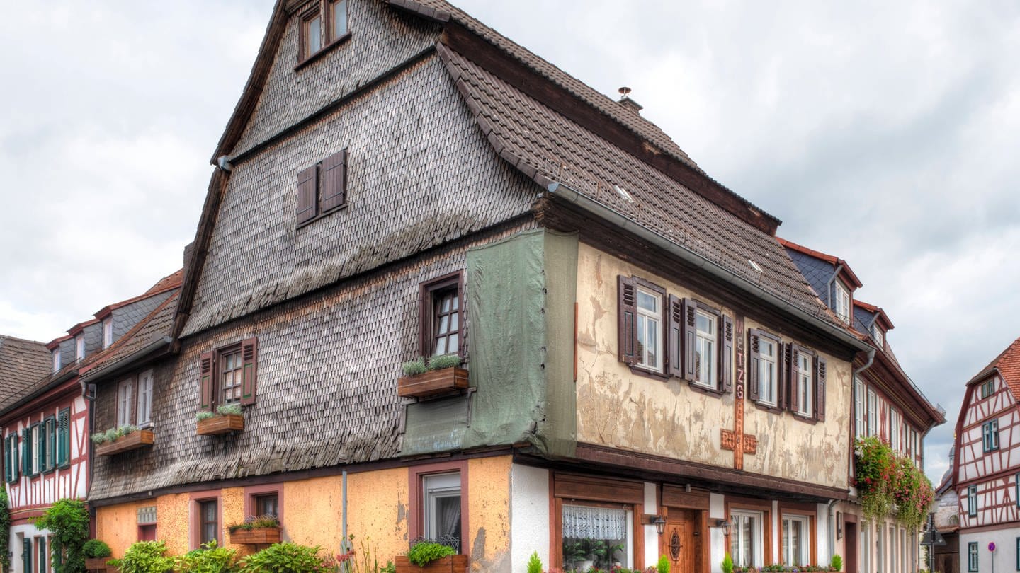 Haus Altes, sanierungsbedürftiges Eck-Wohnhaus in der historischen Altstadt von Seligenstadt, Hessen, Deutschland mit Blumenkübeln an einer gepflasterten Straßenkreuzung