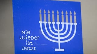 Ein Aufkleber mit der Aufschrift "Nie wieder ist jetzt" und dem Chanukkaleuchter prangt auf einer Tür in Frankfurt als Zeichen gegen Antisemitismus, Hass und Hetze.