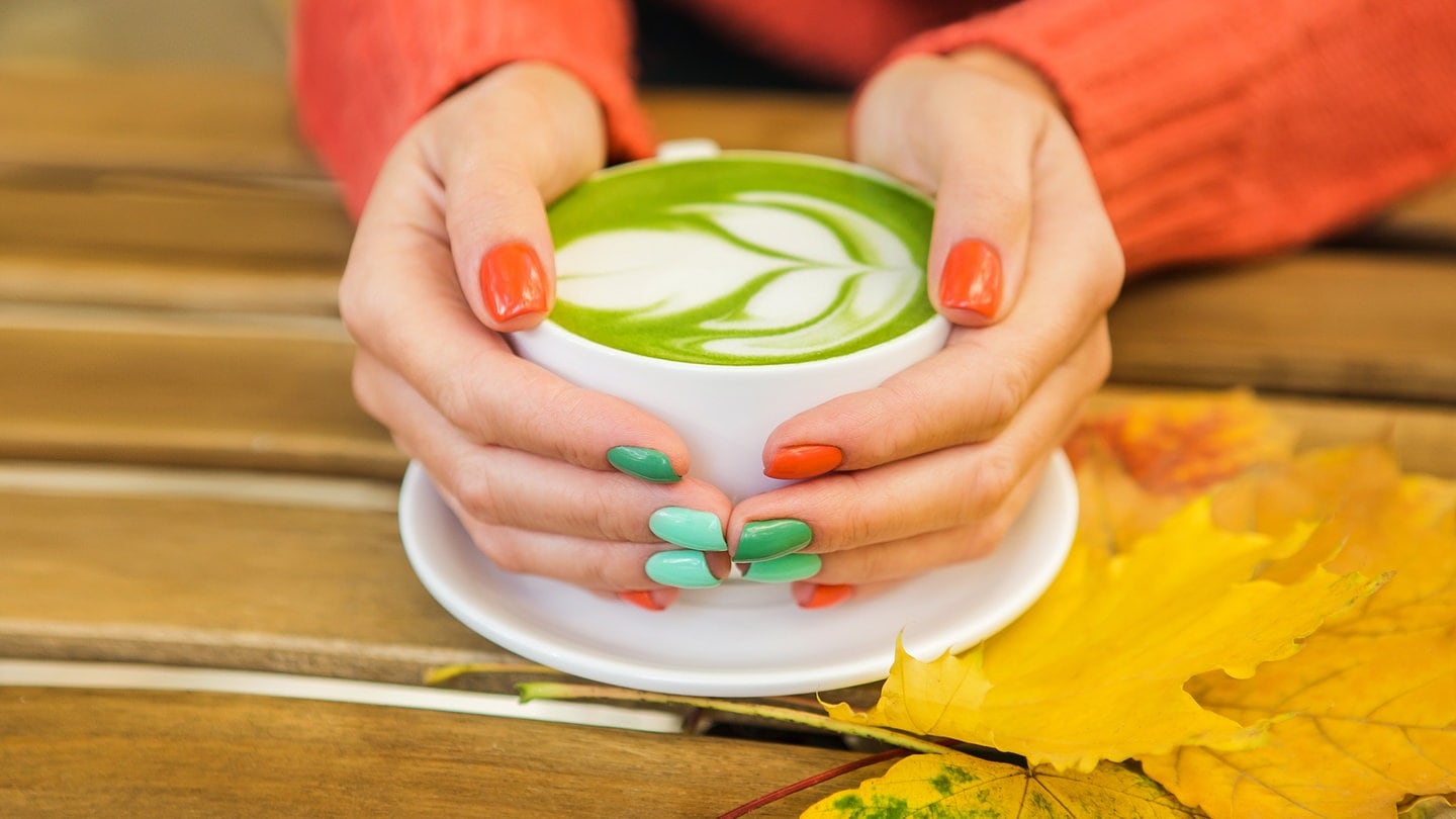 Female hands holding cups of matcha green tea on rustic wooden table background