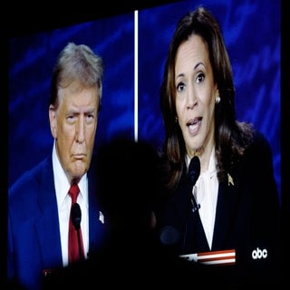 Kamala Harris und Donald Trump sind während des TV-Duells auf einem großen Bildschirm etwas unscharf zu sehen