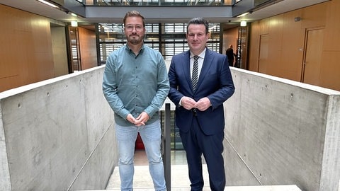 Korrespondent Jim-Bob Nickschas und Hubertus Heil stehen in der Halle im ARD-Hauptstadtstudio nebeneinander und schauen in die Kamera