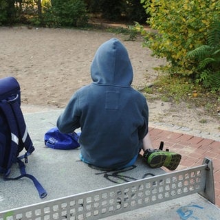 Ein Junge sitzt mit seinem Schulranzen auf einer Tischtennisplatte auf einem Spielplatz