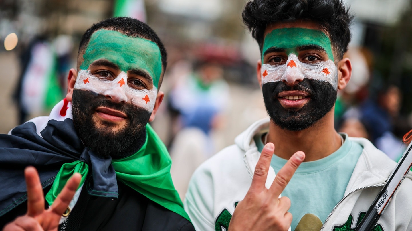 Zwei junge Männer haben sich für eine Kundgebung in Wuppertal eine syrische Flagge ins Gesicht gemalt