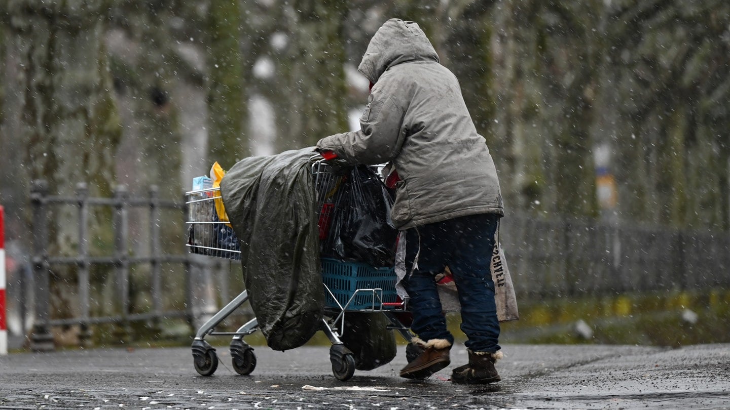 Obdachlose Frau im Regen schiebt einen Einkaufswagen mit ihren Sachen.