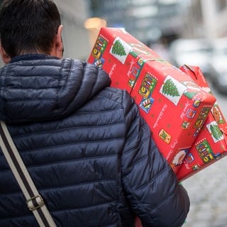 Ein Mann hält Weihnachtsgeschenke im Arm, die er gerade eingekauft hat.