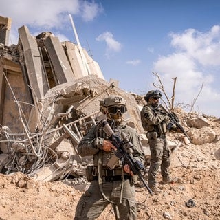 Zwei bewaffnete Soldaten vor einem zerstörten Gebäude.