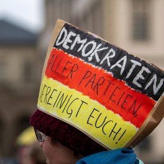 Bei einer Demonstration für Demokratie trägt ein Teilnehmer einen Papphut in Deutschland-Farben und der Aufschrift "Demokraten aller Parteien vereinigt Euch"