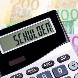 Fotomontage aus einem Taschenrechner mit dem Wort "Schulden" und Geldscheinen. Viele Kommunen in Rheinland-Pfalz sind hoch verschuldet und fordern vom Land eine Reform des kommunalen Finanzausgleichs.