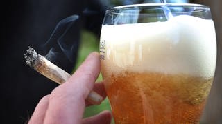 Eine Hand hält einen Joint neben einem Bierglas. 