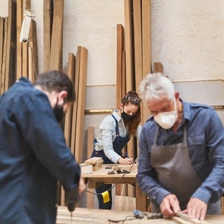 Ein Handwerker Team mit Mundschutz wegen Covid-19 arbeitet in einer TischlereiWerkstatt.