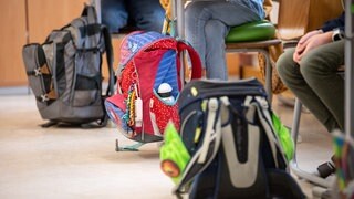 Die Schulranzen von Schülern einer Grundschule sind während des Unterrichts neben den Tischen der Kinder zu sehen.