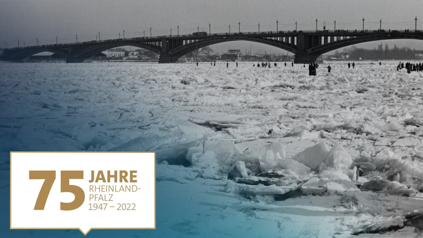 Eisperiode im Februar 1956 in Mainz: Spaziergänger laufen über den zugefrorenen Rhein an der Theodor-Heuss-Brücke - auf dem Bild ein Badge zu 75 Jahre RLP