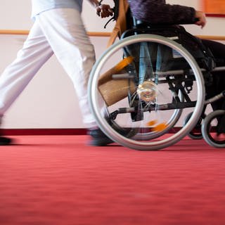 Ein Pfleger eines Pflegeheims schiebt eine Bewohnerin mit einem Rollstuhl. 