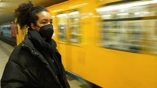 Frau mit FFP2-Maske steht vor Bahn