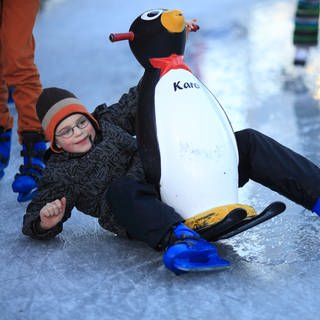Kind mit einer Pinguinfigur beim Eislaufen. In Rheinland-Pflaz öffnen jetzt die Outdoor-Eisbahnen