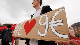 Ein junger Mann hält ein Pappschild hoch mit der Aufschrift "We Love 9 Euro" - der Landtag in RLP diskutiert über Nachfolgemodelle