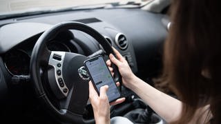 Eine Autofahrerin hat während der Fahrt ihr Handy in der Hand