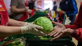 Ein Mensch überreicht einem anderen einen Salatkopf. Immer mehr Menschen in Rheinland-Pfalz sind auf Lebensmittelspenden angewiesen.